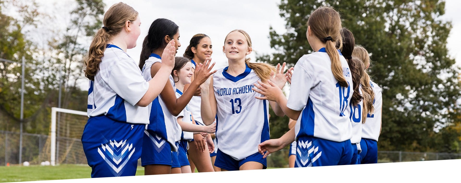A team of girls in blue and white soccer uniforms celebrates and high-fives each other on a field.
